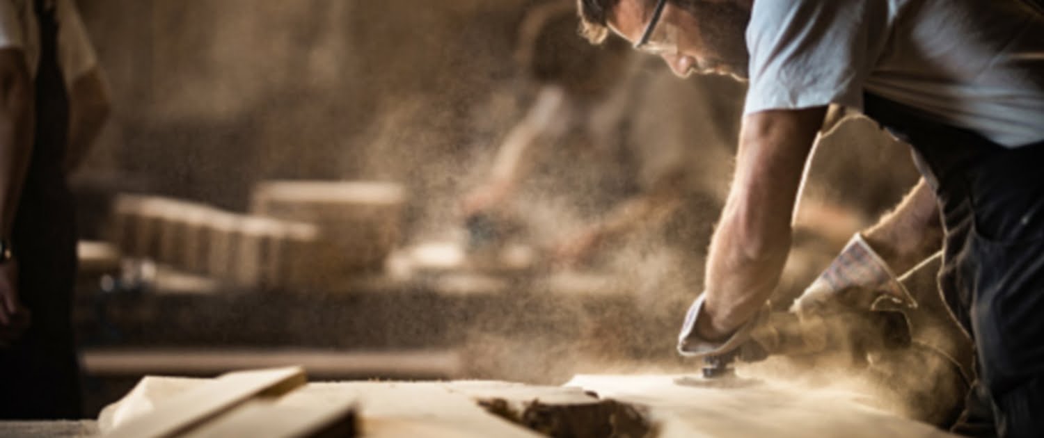Manual worker using sander while working on a wood in carpentry workshop.